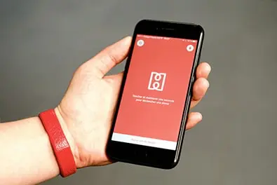 A hand wearing the red HELP bracelet holds an iPhone displaying the app.