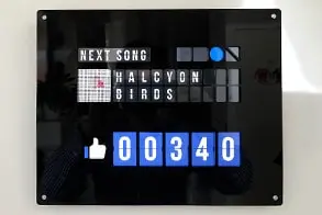 A black enclosure displays an illuminated like counter and the title of the next song.