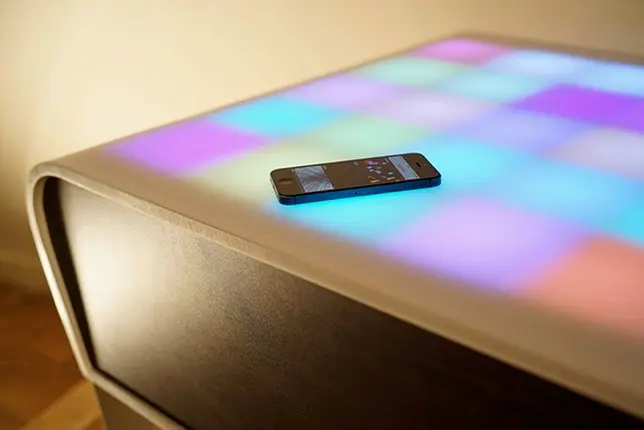 The TA+BLE coffee table with multicoloured illuminated cells and an iPhone on its surface.